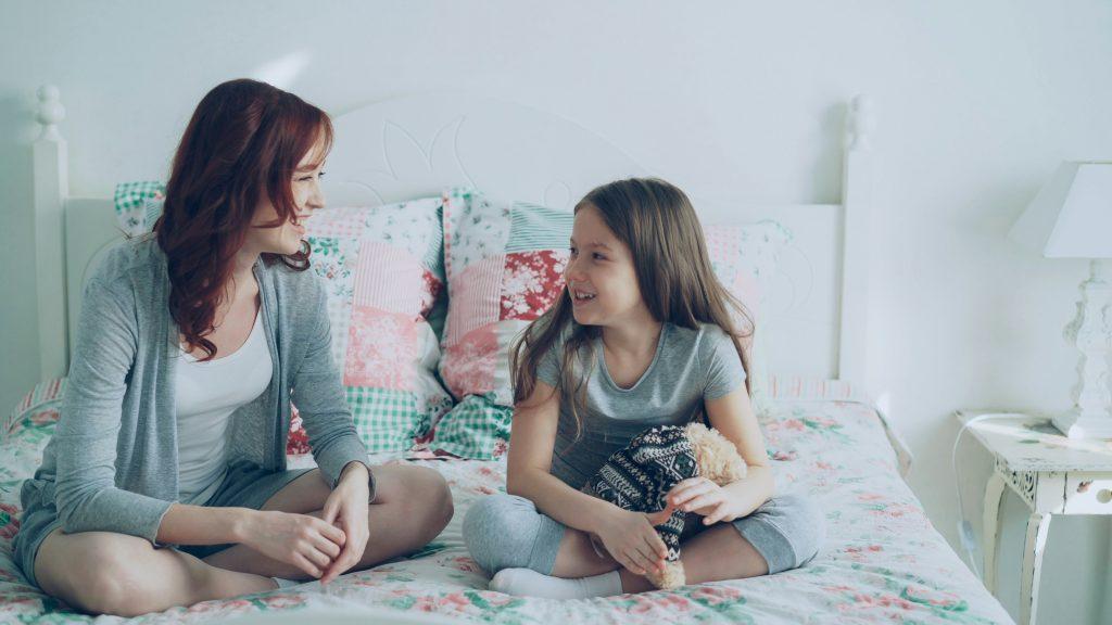 Mother and daughter are sitting on a bed talking