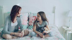 Mother and daughter are sitting on a bed talking